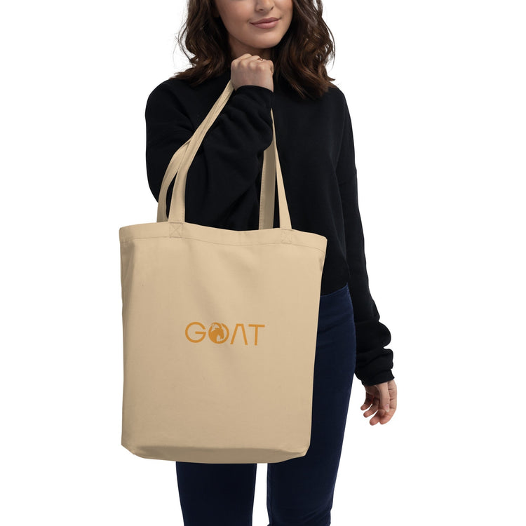 Woman carrying a beige tote bag with the word Goat embroidered.