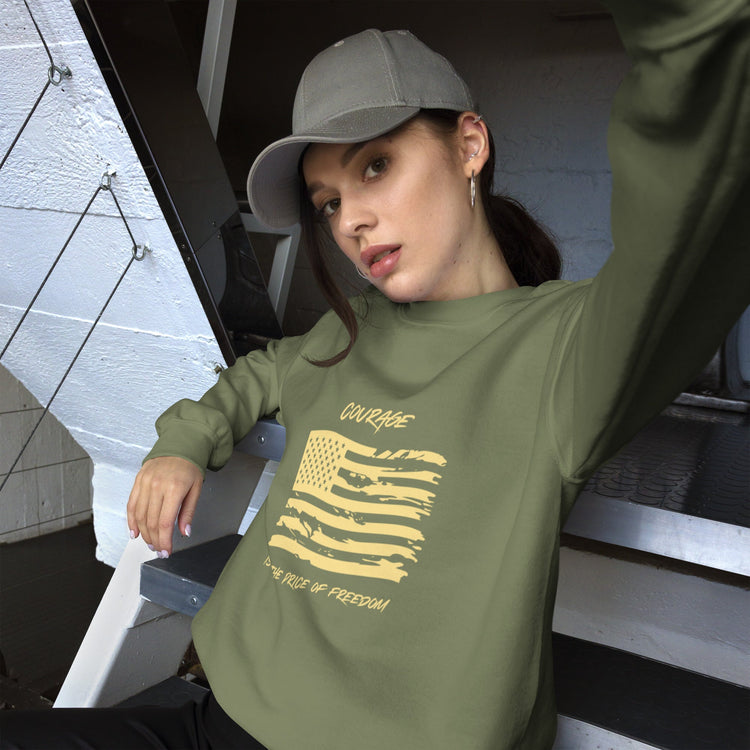 Woman wearing a green sweatshirt with a yellow American flag, gray hat, sitting down.