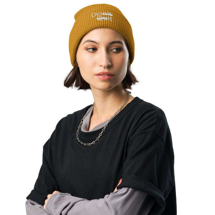 Young woman wearing a gold beanie that says Don't Quit but the n't and Qu are struck out so the message reads Do It